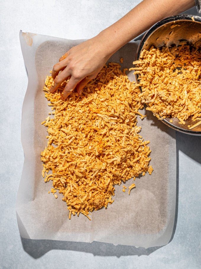 hand spreading shredded tofu on baking sheet