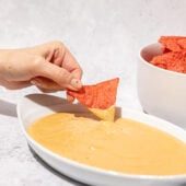 hand dipping chip into vegan queso in white bowl