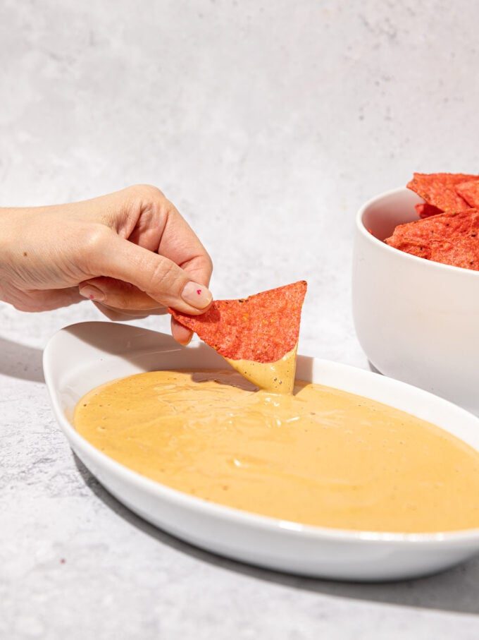 hand dipping chip into vegan queso in white bowl