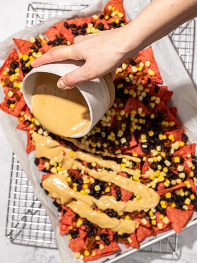 hand pouring cashew queso over nachos