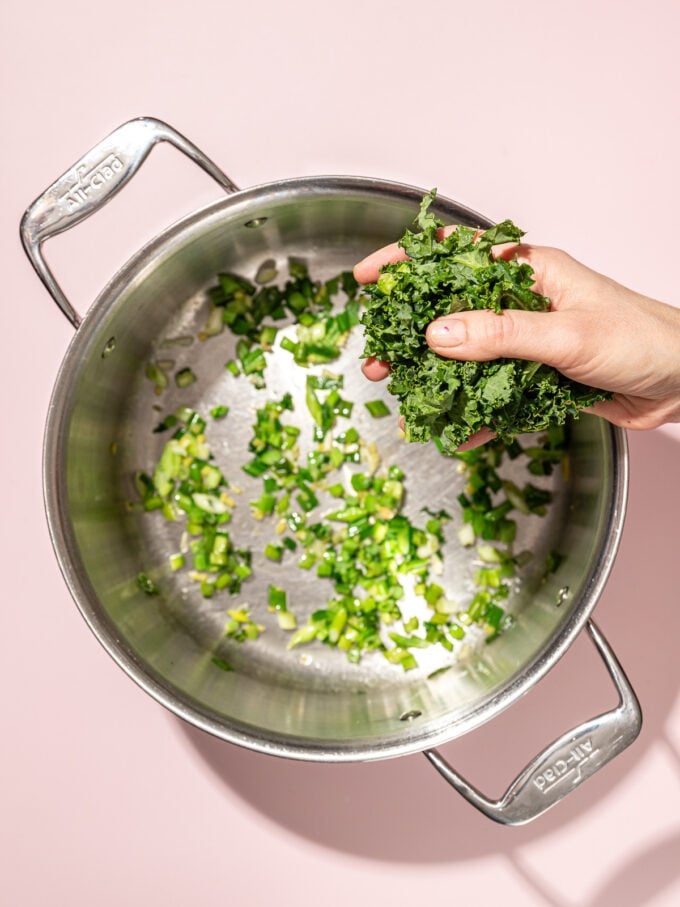 hand adding kale to pot