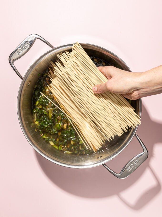 hand adding ramen noodles to pot