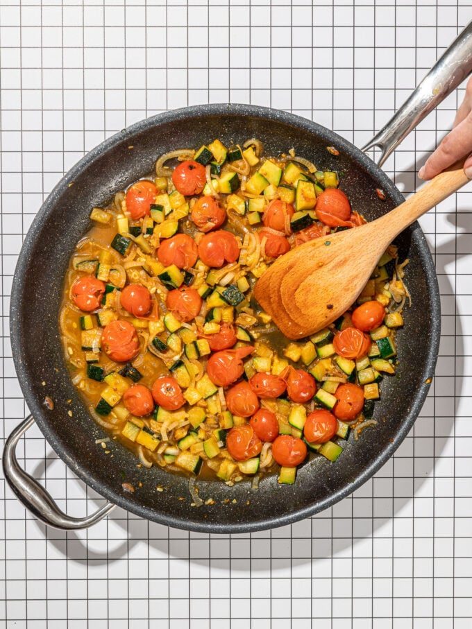 wooden spoon and tomato zucchini in skillet