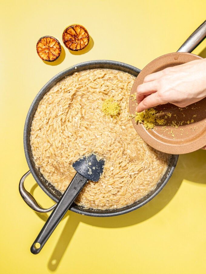 Hand adding lemon zest to orzo