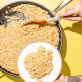 hand scooping lemon orzo onto plate