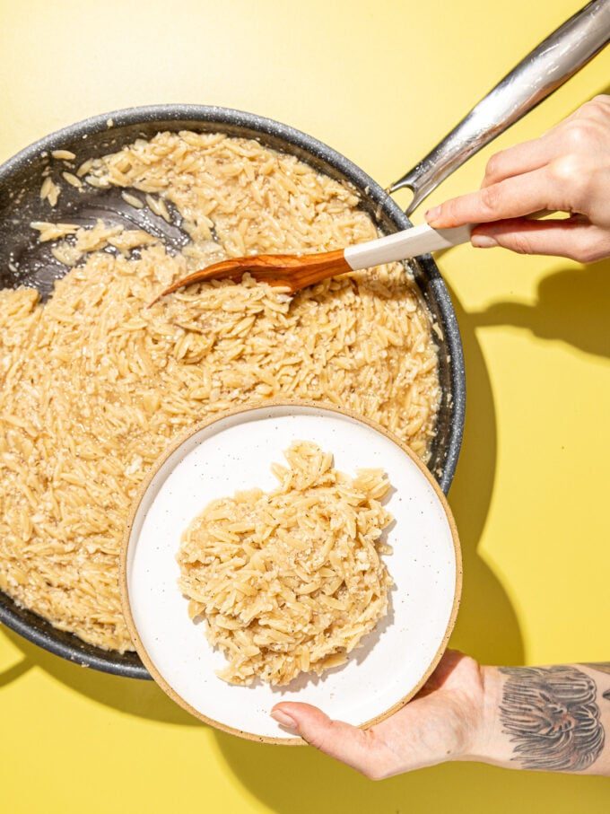 hand scooping lemon orzo onto plate