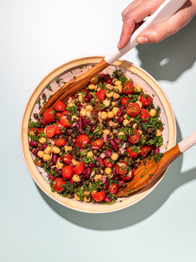 hands tossing bean salad with wooden spoons