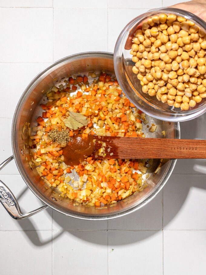 pouring chickpeas into soup pot with veggies
