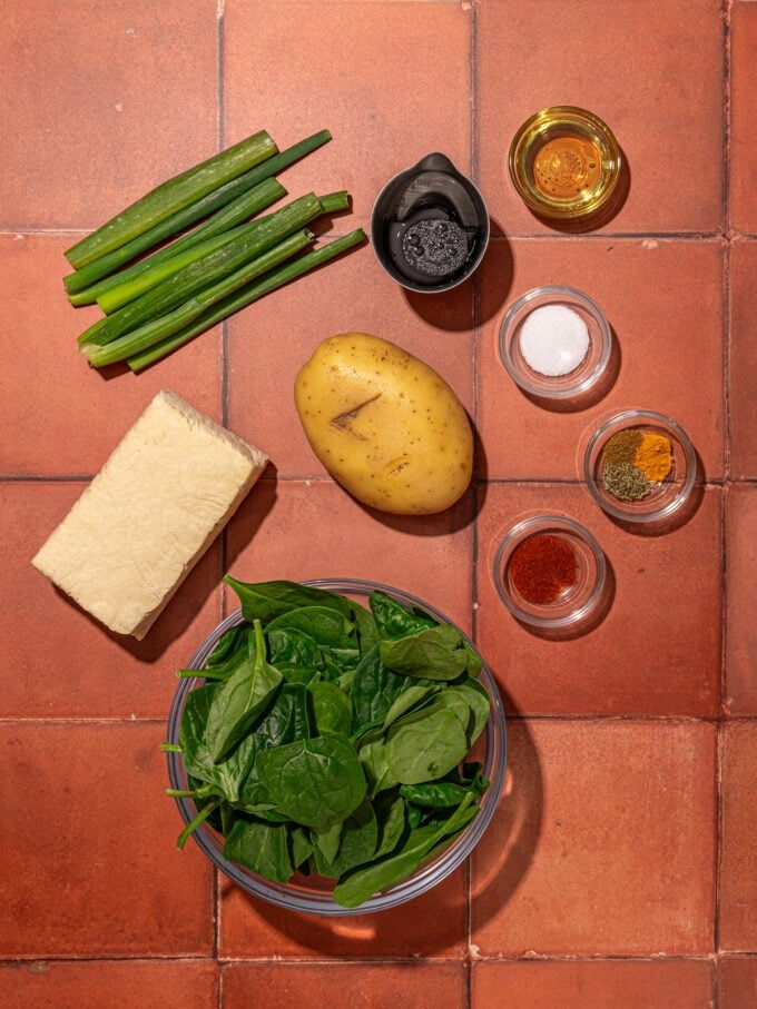 spinach, tofu, potato and green onions on a brick background
