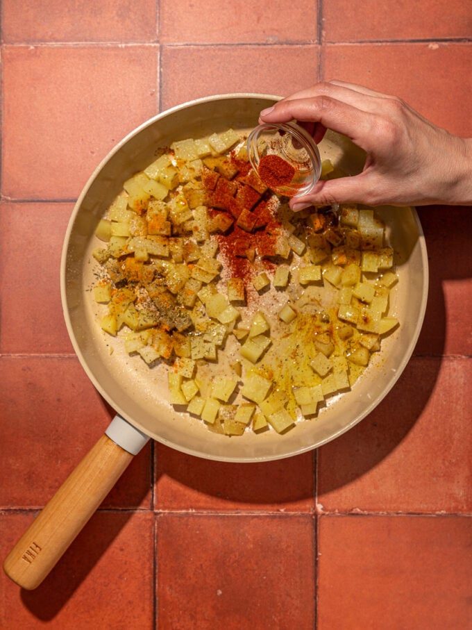 hand pouring paprika onto potatoes in skillet