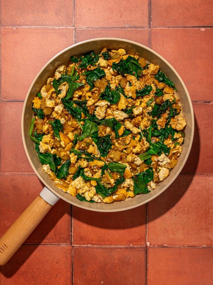 tofu, spinach and potatoes in a skillet on red brick