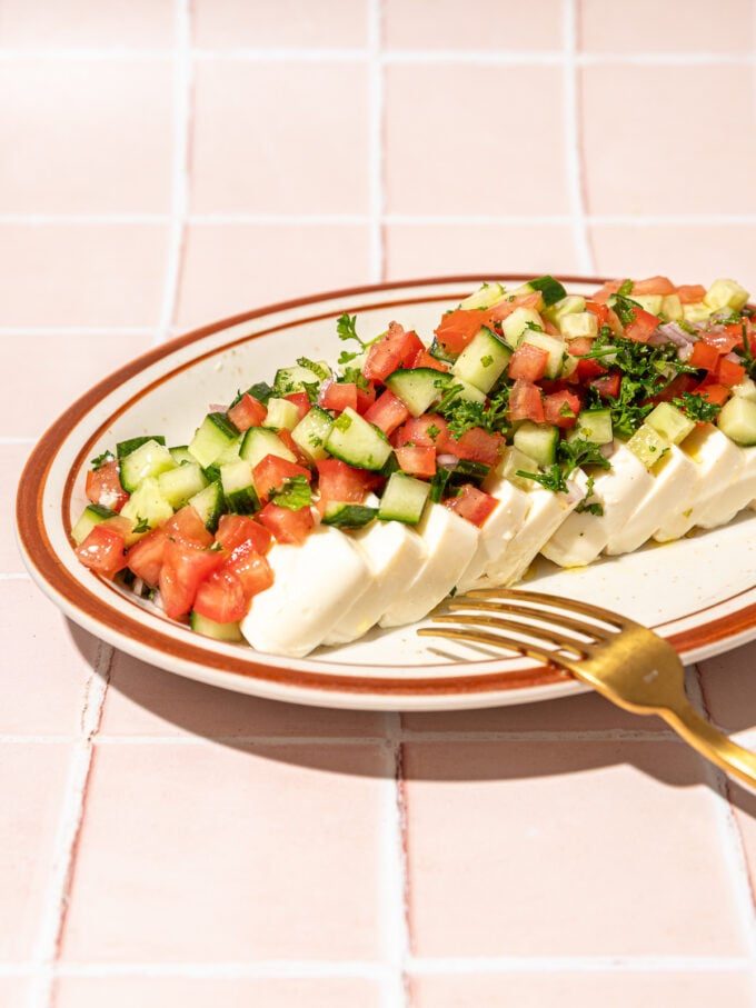 sliced tofu, diced tomato and cucumber on plate with fork on pink tiles
