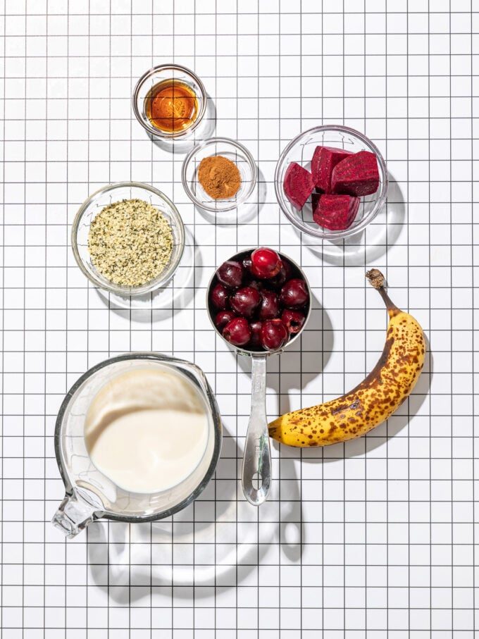 bowls of milk, cherries, hemp hearts, beets and a banana on black and white grid