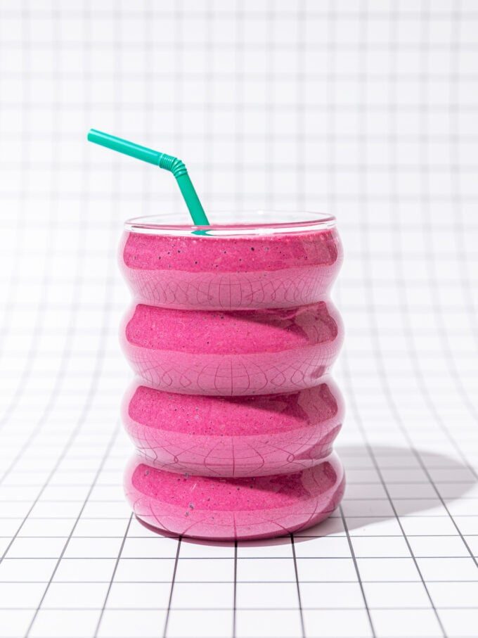 pink smoothie with green straw on black and white tiles