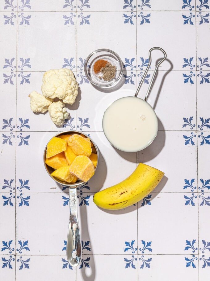 cauliflower, mango, banana, milk and spices on white and blue tile background